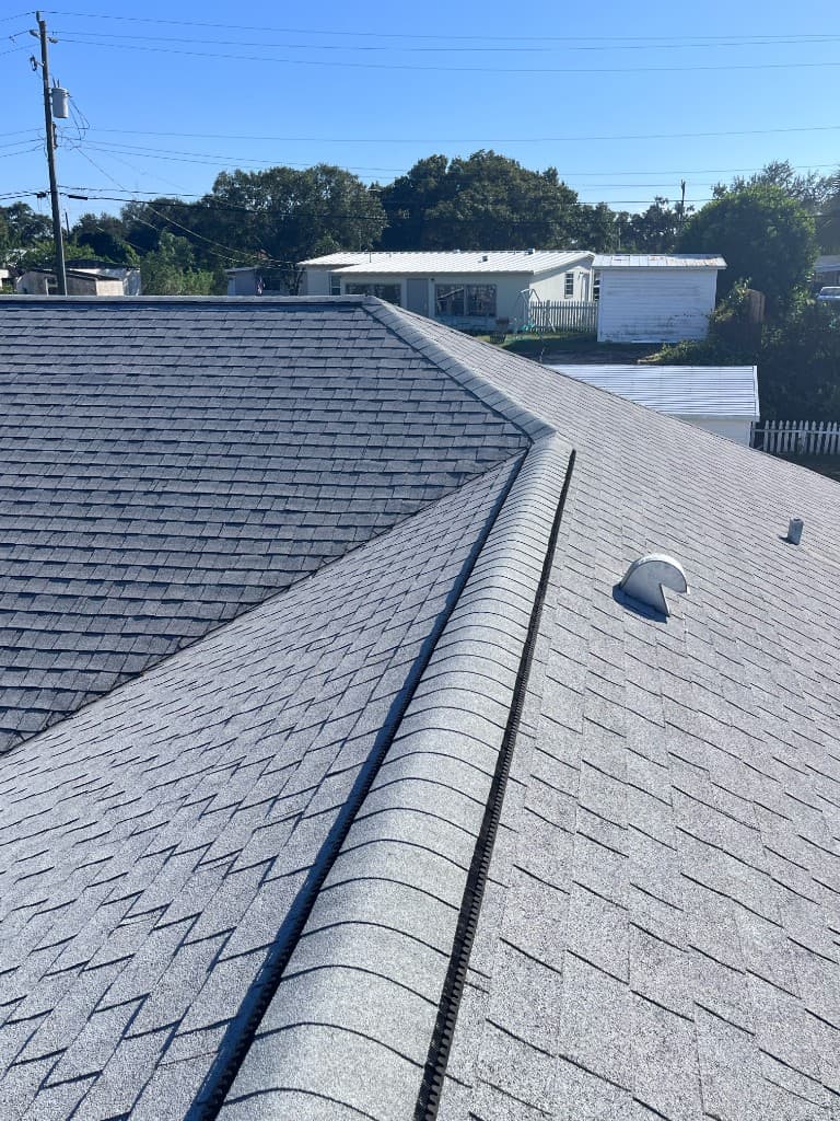 A close view of architectural shingles, the ridge cap, and a pipe flashing on a residential roof