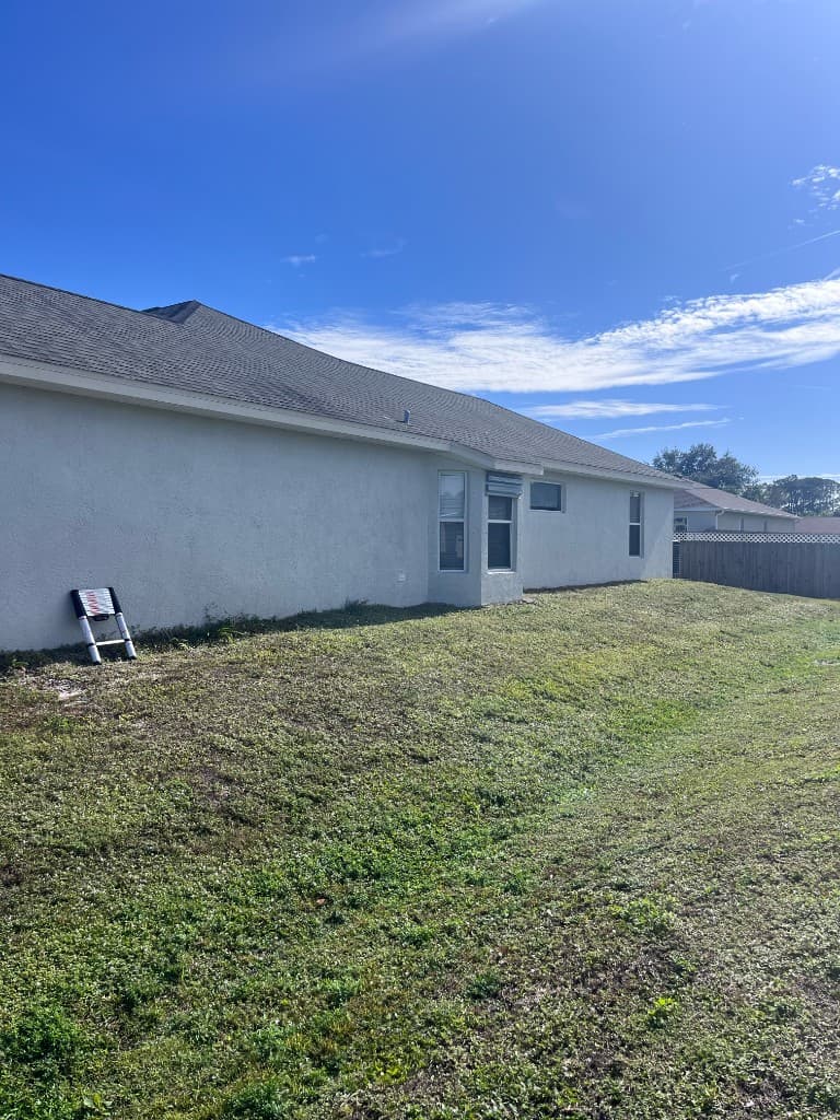 The long side of a stucco house and its gray shingle roof against a bright sky